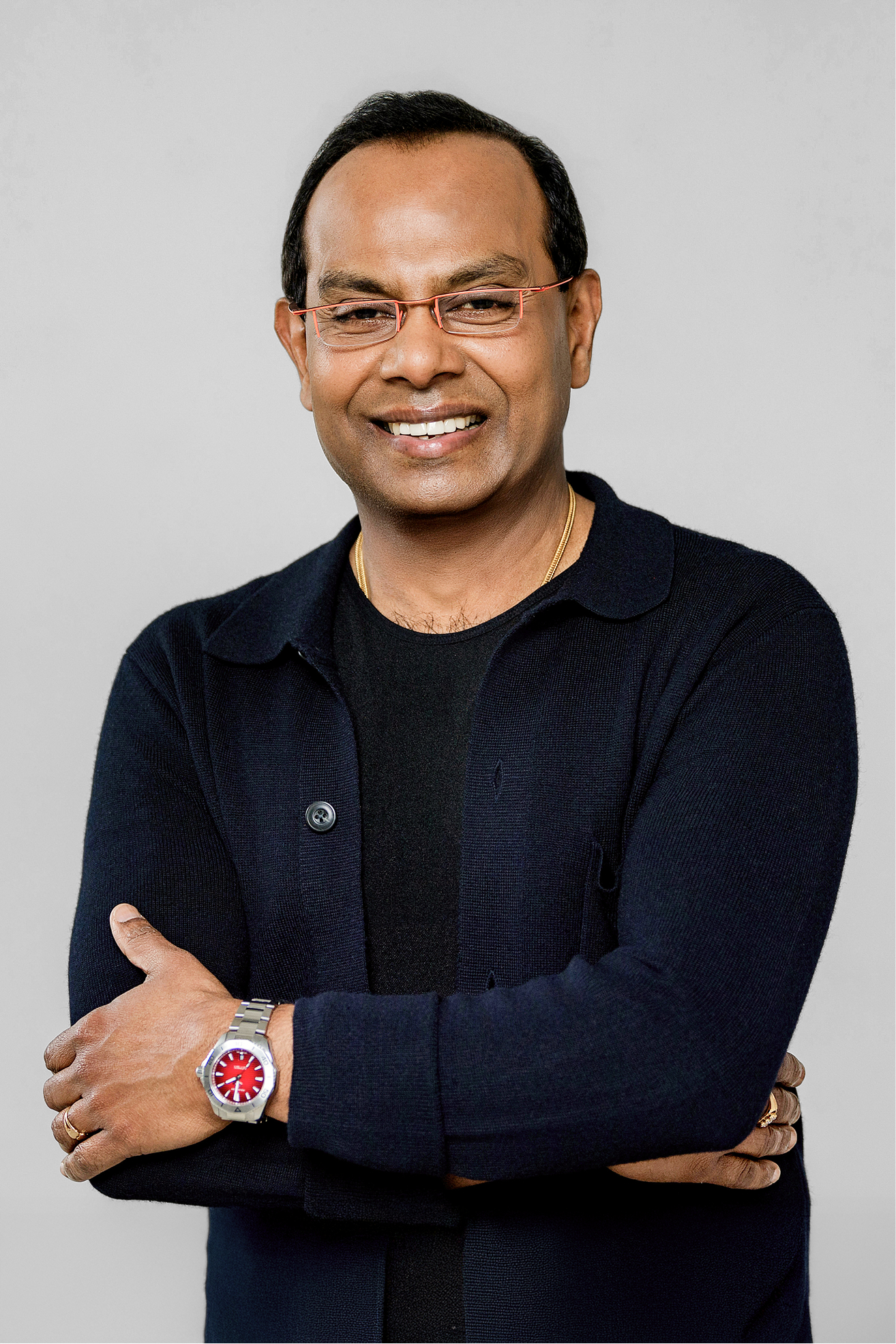 Smiling man with red-framed glasses wearing a navy cardigan, arms crossed, facing the camera.